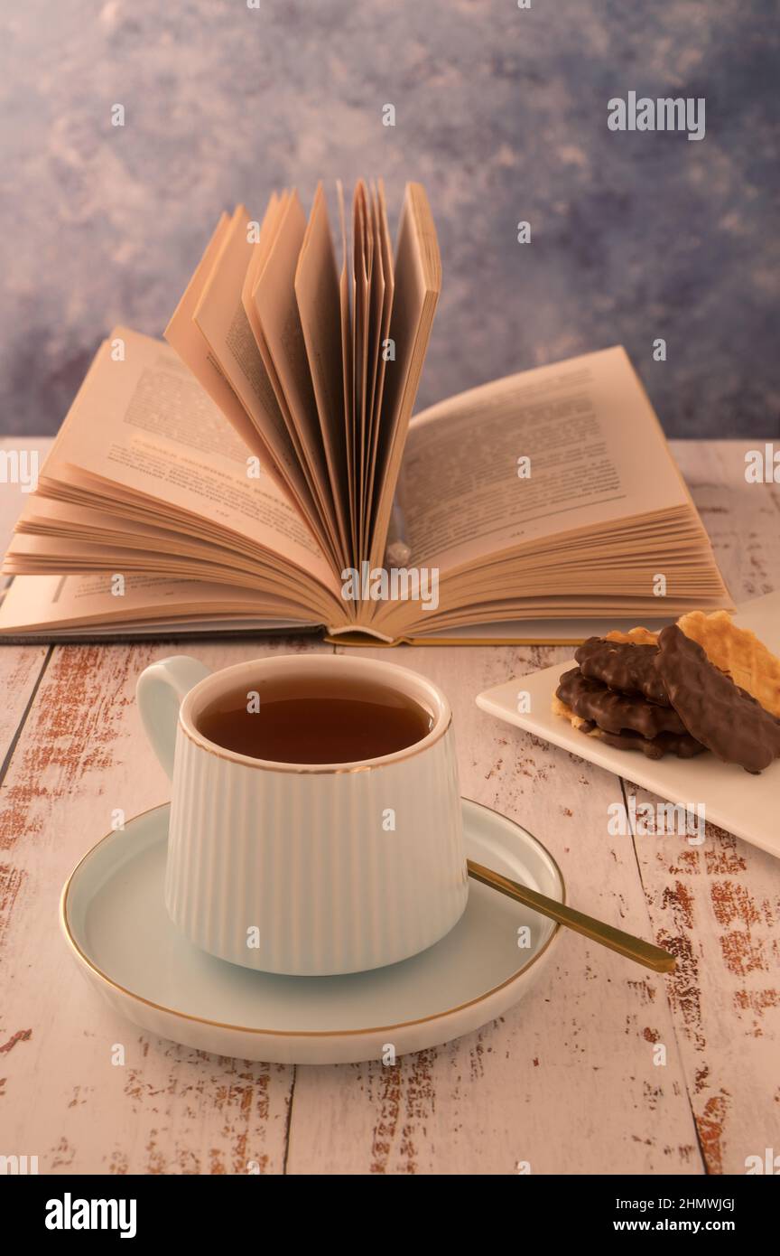 Une grande photo de la relaxation matinale se fait dans des couleurs chaudes. Une tasse de thé et un livre est le meilleur début de journée. Une ambiance romantique vous permettra d'améliorer votre atmosphère Banque D'Images
