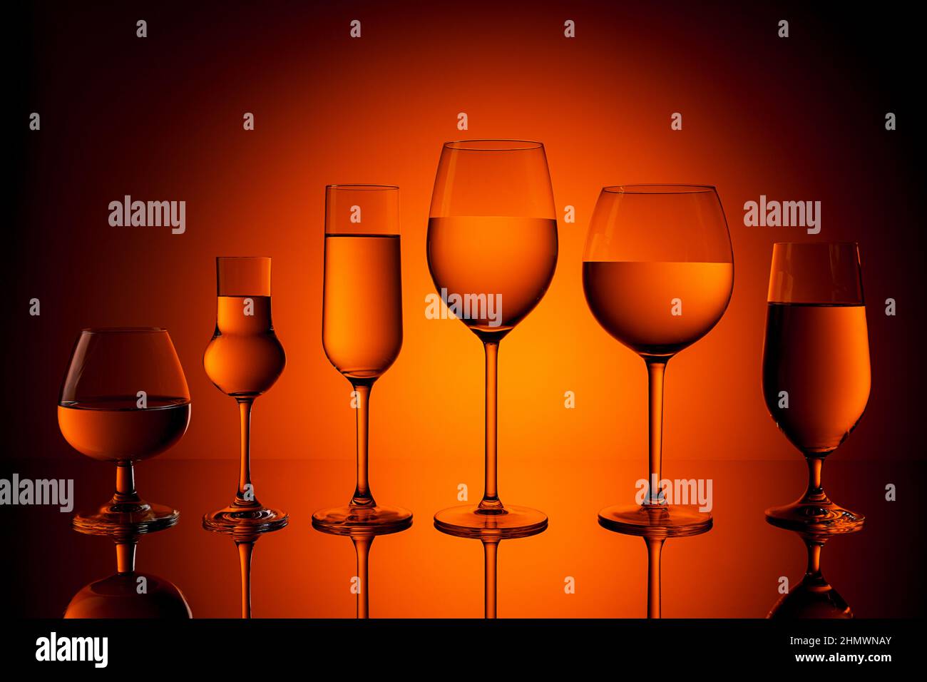 Une rangée de plusieurs verres de vin, Whiskey, Grappa, champagne et bière sur fond de coucher de soleil orange. Prise en Studio avec un 5D Mark III Banque D'Images