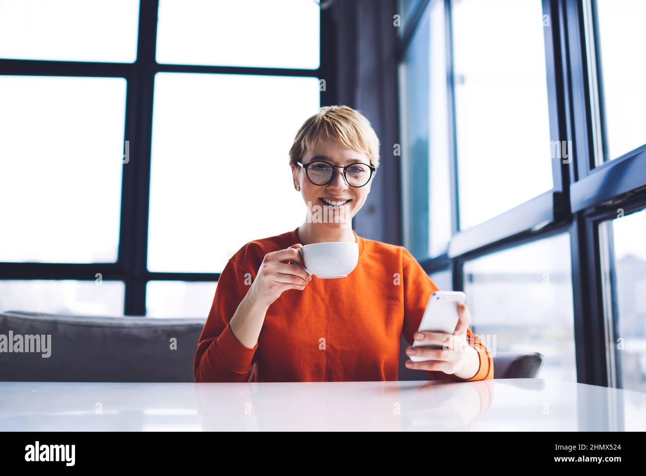 Femme souriante buvant un café sur smartphone Banque D'Images
