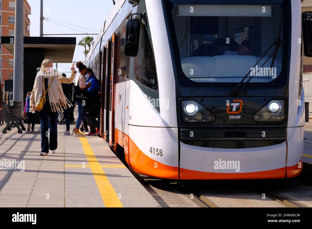 villajoyosa Alicante Espagne 02.12.22 un train électrique blanc et orange attend un arrêt de ville. Les passagers montent et descendez du tramway. Une jeune femme portant un masque Banque D'Images villajoyosa Alicante Espagne 02.12.22 un train électrique blanc et orange attend un arrêt de ville. Les passagers montent et descendez du tramway. Une jeune femme portant un masque Banque D'Images