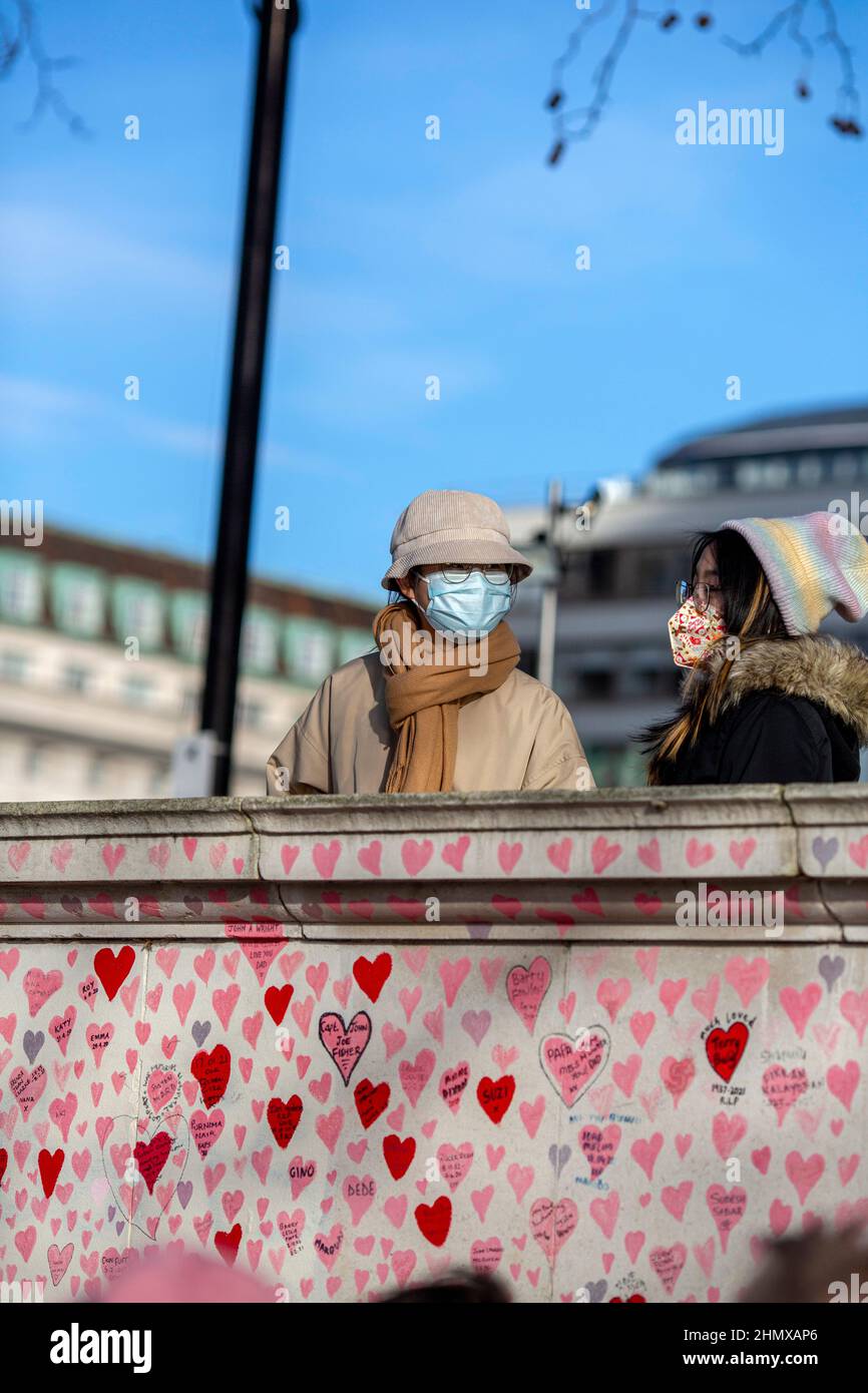 Touristes asiatiques avec masque regardant le mur commémoratif national COVID peint avec des coeurs rouges sur beau jour ensoleillé. Westminster, Londres, Royaume-Uni Banque D'Images