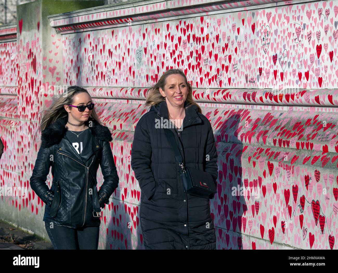 À la femme passant le mur commémoratif national de COVID peint avec des coeurs rouges sur beau jour ensoleillé . Westminster, Londres , Royaume-Uni . Banque D'Images