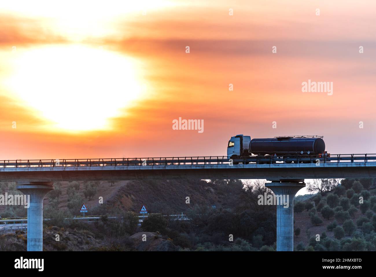 Camion-citerne avec des marchandises dangereuses circulant sur un pont au coucher du soleil. Banque D'Images