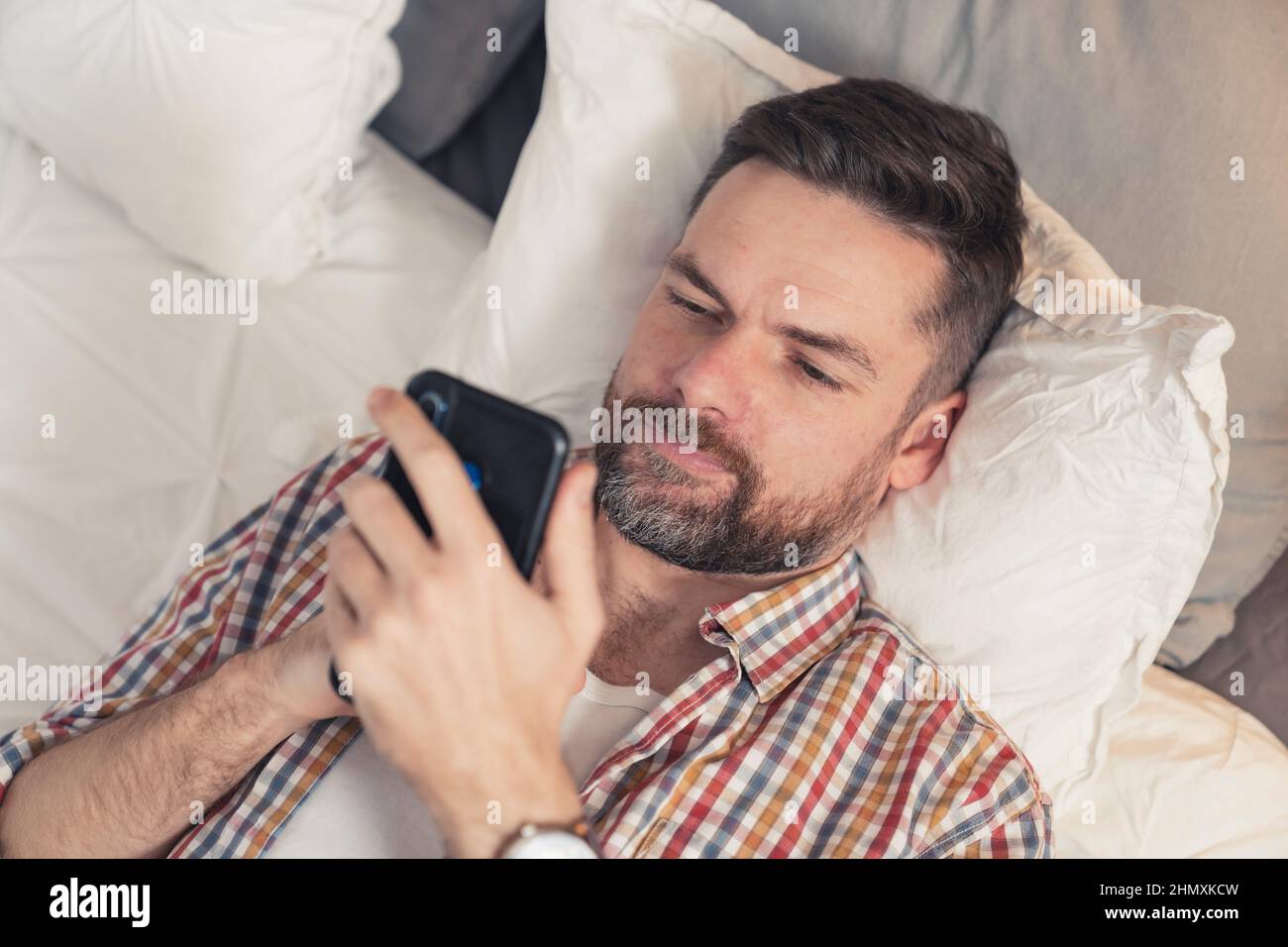 une lad caucasienne avec une barbe complète lisant un article sérieux en ligne en utilisant son nouveau smartphone noir. Photo de haute qualité Banque D'Images