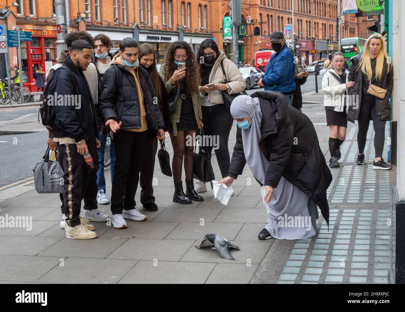 Une étudiante française voilée vêtue de hijab et portant un masque chirurgical tente d'attraper un pigeon blessé à Grafton Street, Dublin Banque D'Images