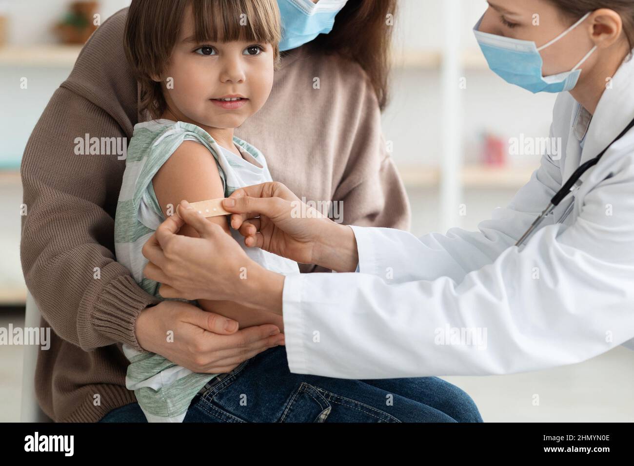 Femme médecin mettant du plâtre médical dans le bras du patient de garçon après l'injection de vaccination contre le covid-19 pendant une pandémie Banque D'Images