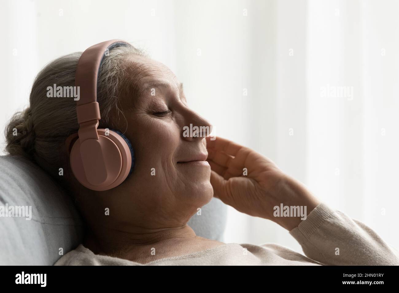 Bonne femme âgée dans un grand casque reposant sur un canapé confortable Banque D'Images