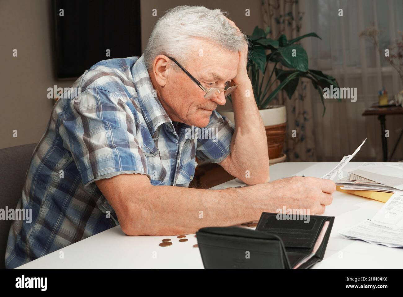 Contrarié déprimé senior homme assis à la table et calculant les finances. Le vieil homme vérifie les factures. Homme comptant des pièces sur la table. Calcul de la pension Banque D'Images