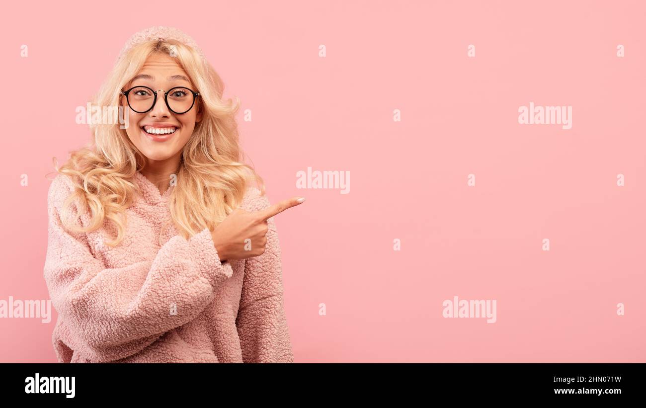 Une jeune femme blonde stupéfait de se mettre à côté de l'espace de copie, montrant un lieu pour une publicité ou un texte promotionnel, fond rose Banque D'Images