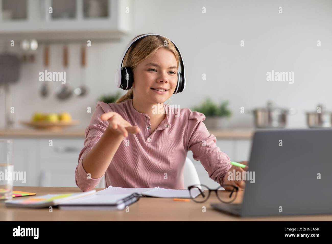 Jeune fille blonde européenne souriante dans les gestes de casque et d'étude à la maison regarder à l'ordinateur portable Banque D'Images