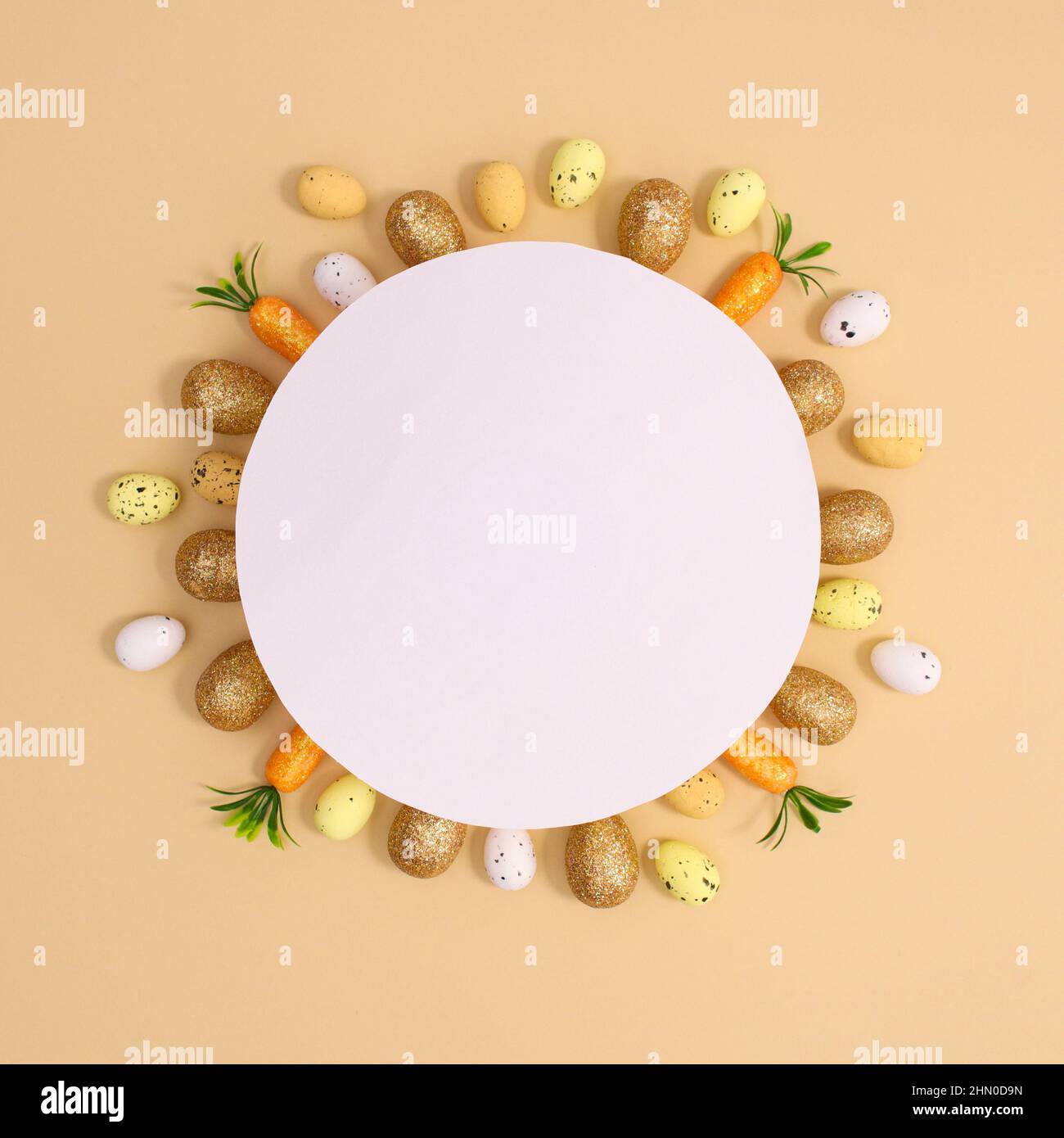 Carte papier pour Pâques avec petits œufs blancs et dorés jaunes et carottes autour du papier sur fond beige pastel. Pose à plat Banque D'Images