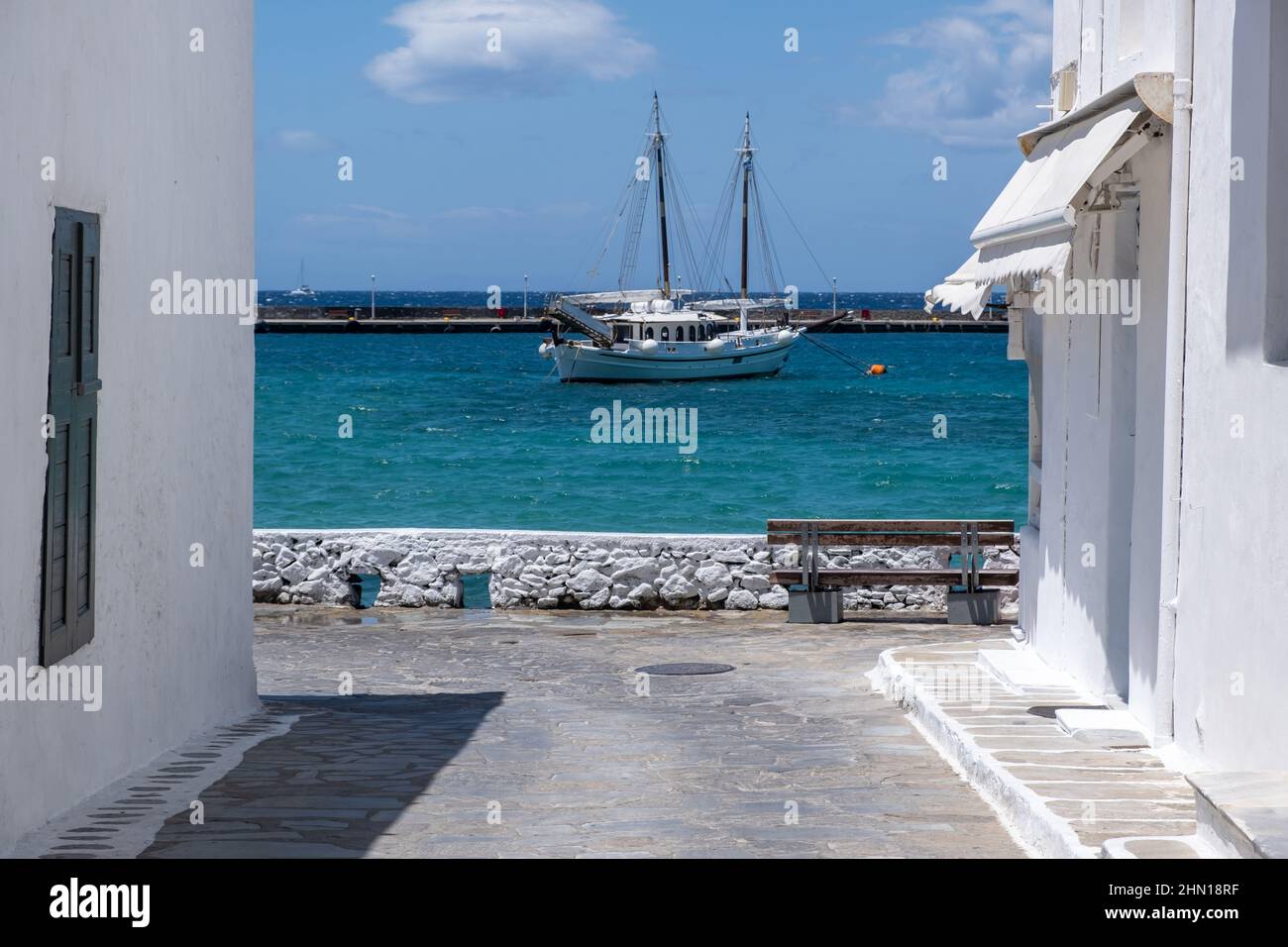 Mikonos, Cyclades, Grèce. Vue sur un bateau amarré dans la mer Égée, entre le front de mer blanchi à la chaux du bâtiment de Mykonos, fond bleu ciel. Le summe Banque D'Images