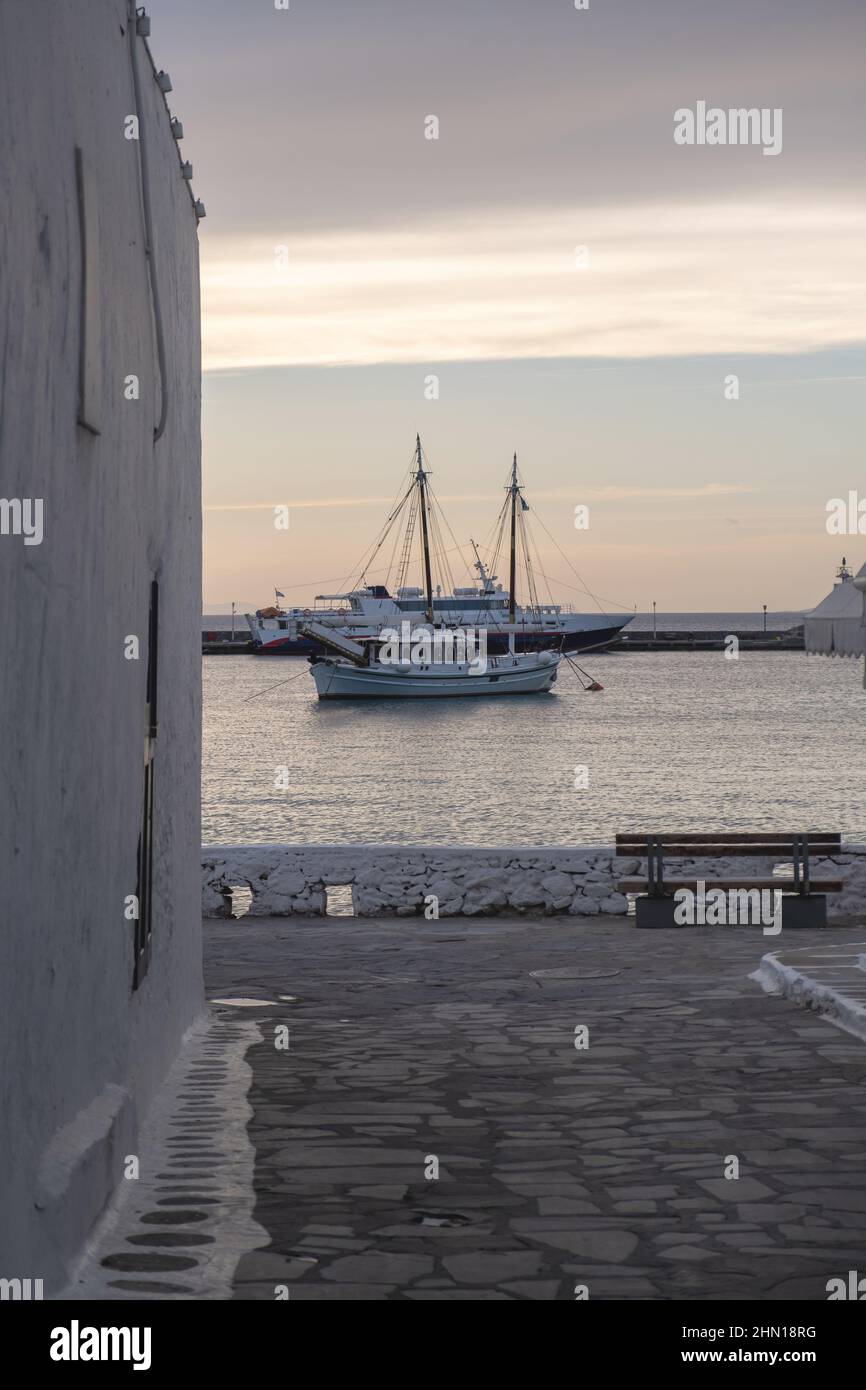 Île de Mykonos, Cyclades, Grèce. Bateau amarré dans la mer au port de Mikonos, vue de côté de mur de bâtiment blanchi à la chaux, banc vide ciel bleu fond Banque D'Images Île de Mykonos, Cyclades, Grèce. Bateau amarré dans la mer au port de Mikonos, vue de côté de mur de bâtiment blanchi à la chaux, banc vide ciel bleu fond Banque D'Images