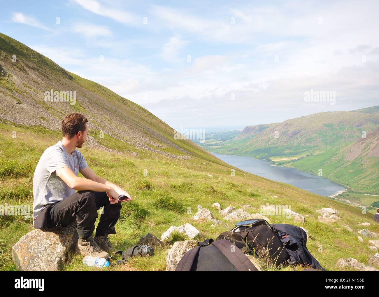 Randonneur en train de faire une pause tout en grimpant en montagne. Scafell Pike, Lake District, Royaume-Uni, vue vers Wast Water. Vue panoramique sur la montagne vers le lac avec de l'herbe Banque D'Images