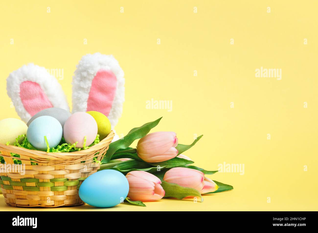 Composition de Pâques. Oeufs dans un panier tulipes oreilles de lapin sur fond jaune. Banque D'Images