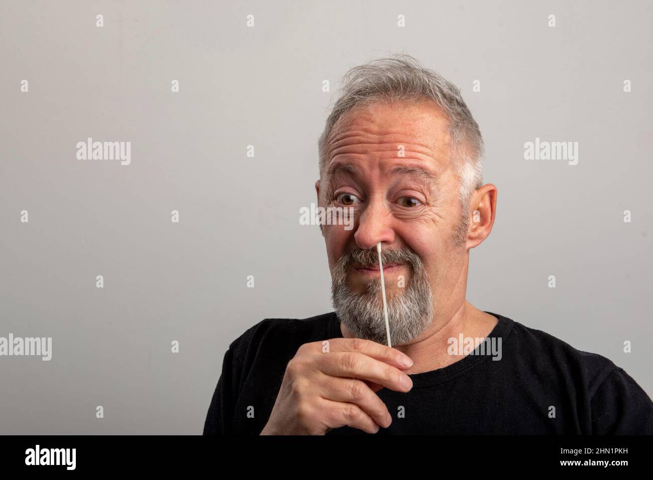 homme d'âge moyen avec cheveux gris et barbe utilisant le coronavirus (covid-19) kit d'auto-test rapide (atk) à la maison avec un coton-tige nasal Banque D'Images