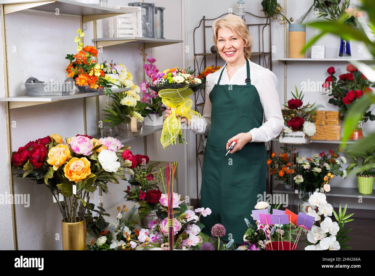 Fleuriste femelle portant un tablier et préparant des fleurs avec joie Banque D'Images