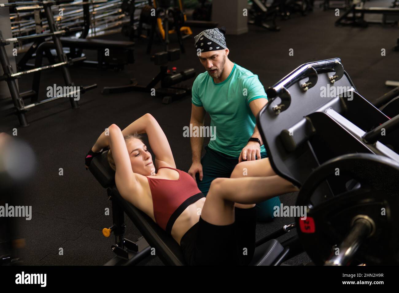 L'entraînement dirigé par un instructeur aide un beau client à effectuer des exercices dans un club de remise en forme, le concept de jouer du sport avec un loisir professionnel de gym Banque D'Images