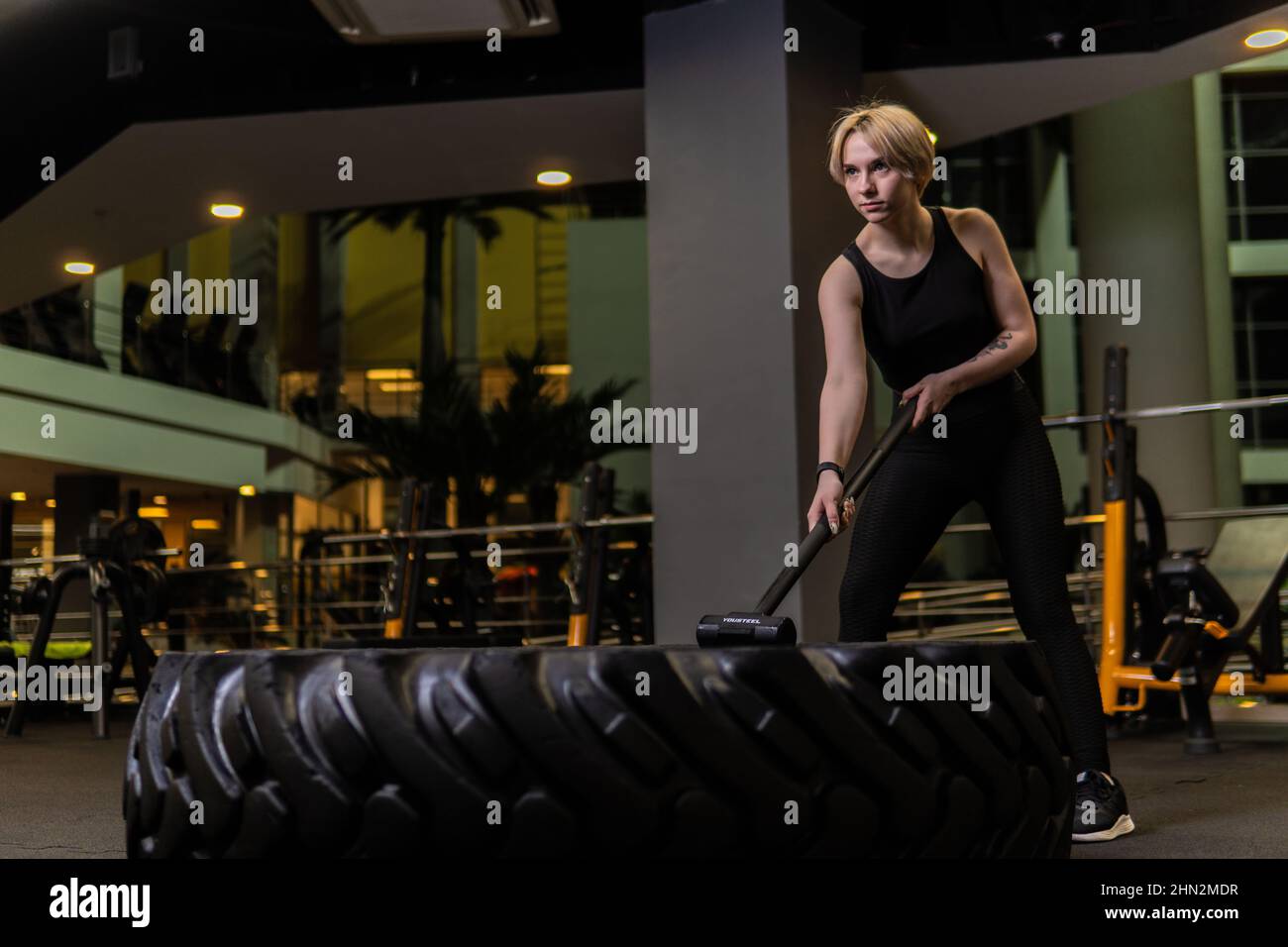 Roue avec sledgehammer fille stands pneu gym exercice, pour la force forte pour le style de vie de traîneau athlétique, tenant pendu. Les muscles posent noir, repos Banque D'Images