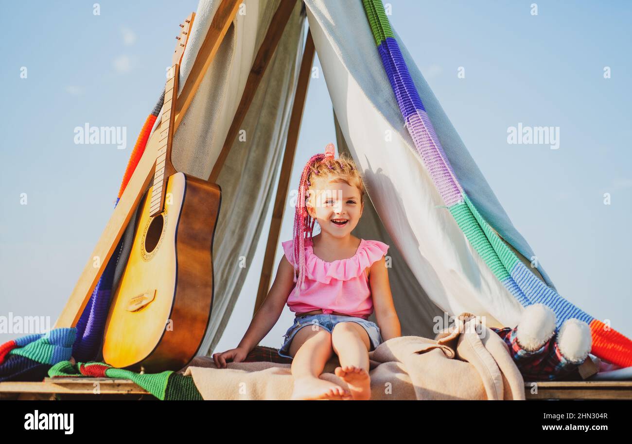 Un enfant souriant dans une tente. Fille jouant dans le camp. Camping pour enfants. S'amuser à l'extérieur. Terrain de camping. Banque D'Images