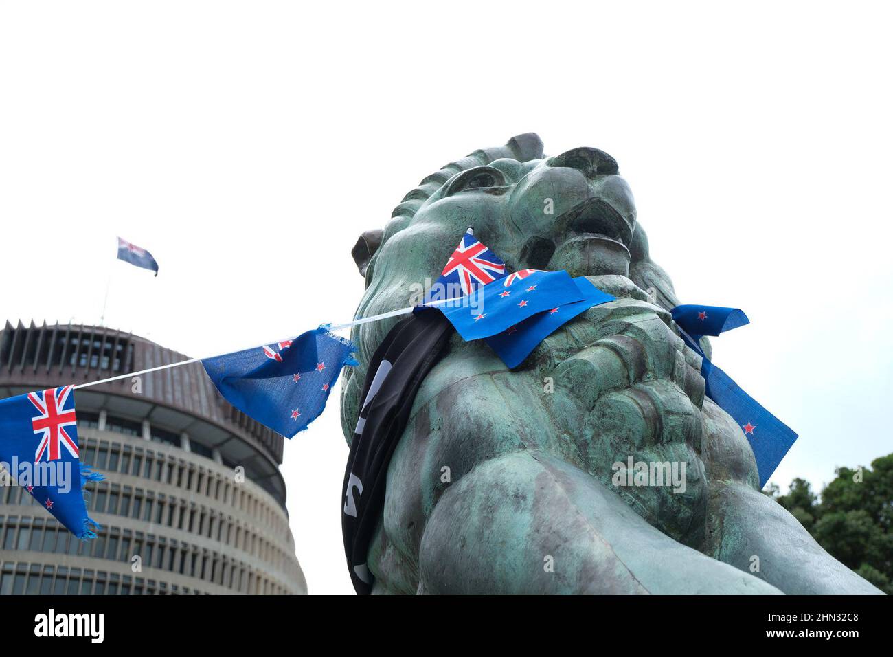 Wellington, Nouvelle-Zélande. 14 février 2022 : une statue d'un lion à l'extérieur du monument commémoratif de guerre sous la ruche est décorée de drapeaux néo-zélandais alors que l'occupation des lieux du Parlement en signe de protestation contre les mandats d'emploi de vaccins Covid-19 et les restrictions imposées aux personnes non vaccinées entre dans sa septième journée. Crédit : Lynn grief/Alamy Live News Banque D'Images