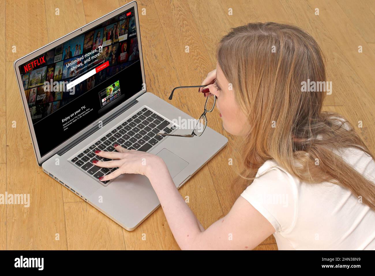 Jeune femme sur le sol à la maison en utilisant le service de streaming Internet d'ordinateur portable navigation page d'accueil Netflix choisir le film à regarder pendant le verrouillage de coronavirus. Banque D'Images