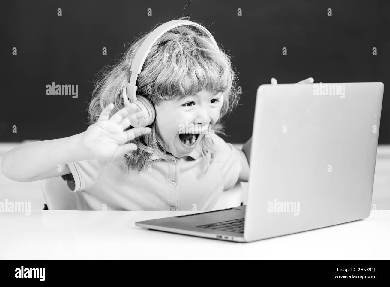 Mignon garçon portant un casque, étudier avec un ordinateur portable dans la salle de classe, écouter le cours de leçon audio.Excitée émotions des enfants. Banque D'Images