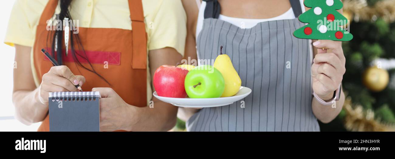 Les femmes serveuses tiennent une assiette de fruits et écrivent la commande près de la fermeture de l'arbre du nouvel an Banque D'Images