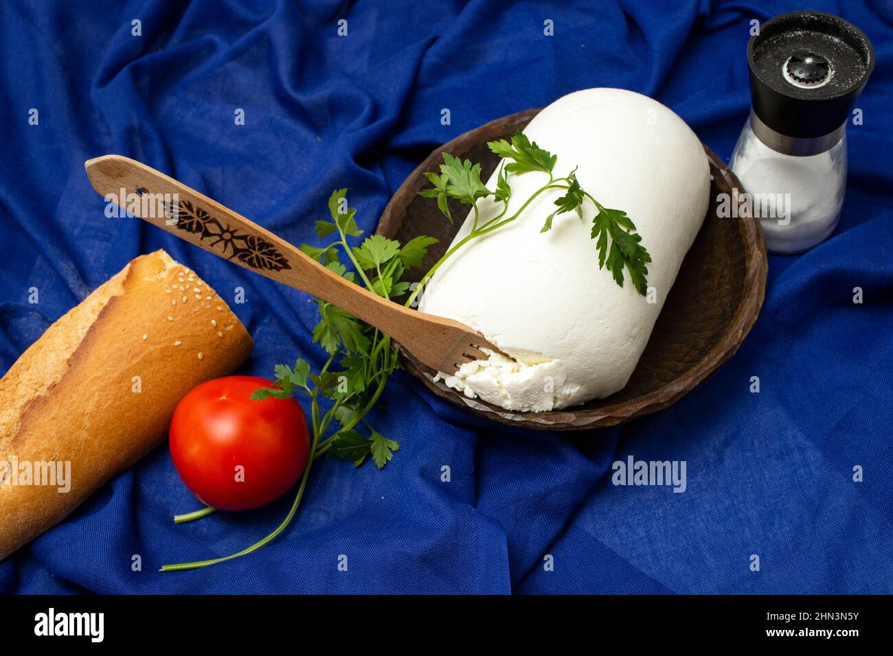Fromage de fermier sur un bol en bois avec du sel, de la tomate et une baguette Banque D'Images