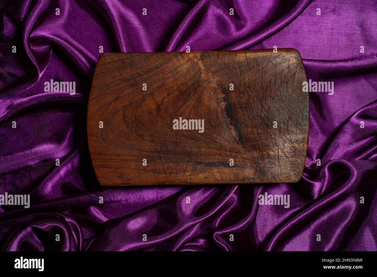 planche à découper en bois sur fond de vagues de satin violet vue du dessus Banque D'Images