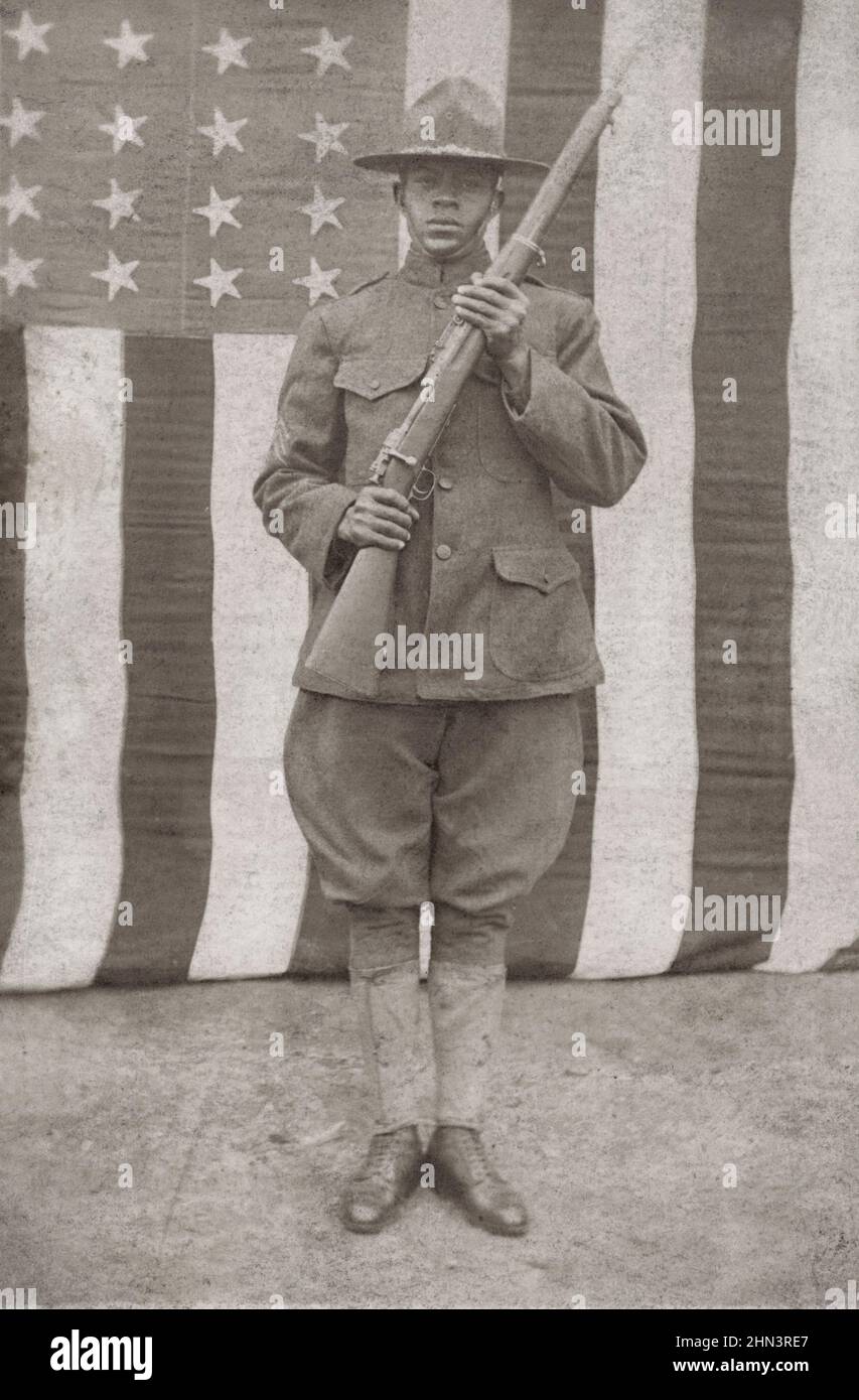 USA pendant la première Guerre mondiale. Soldat américain africain en uniforme et chapeau de campagne avec fusil devant le drapeau américain. 1917-1918 Banque D'Images