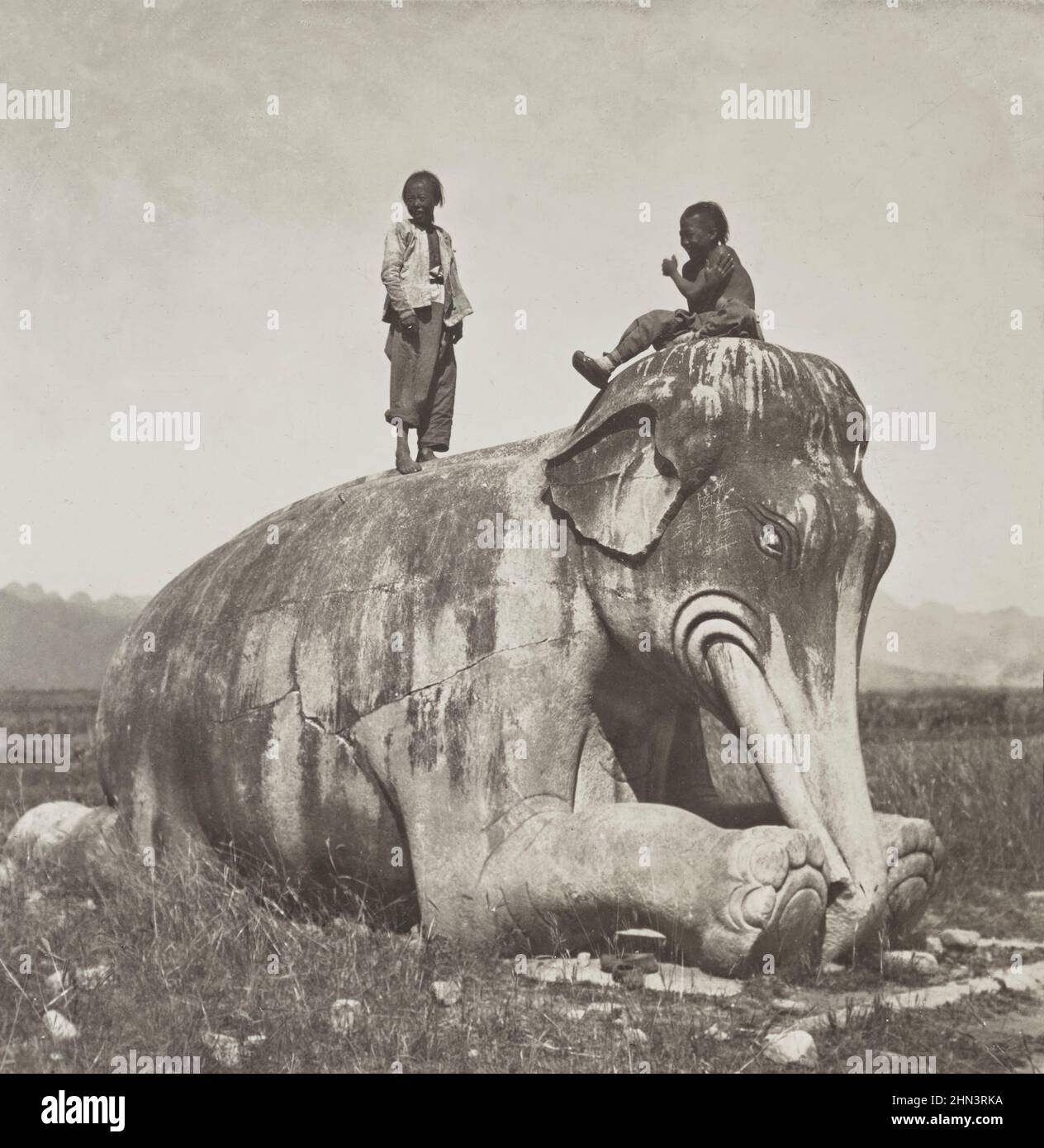 Photo d'époque des enfants chinois avec file d'attente au-dessus des statues d'éléphants à genoux dans l'avenue des animaux de pierre, les tombes de Ming. Chine du Nord. Juillet 190 Banque D'Images