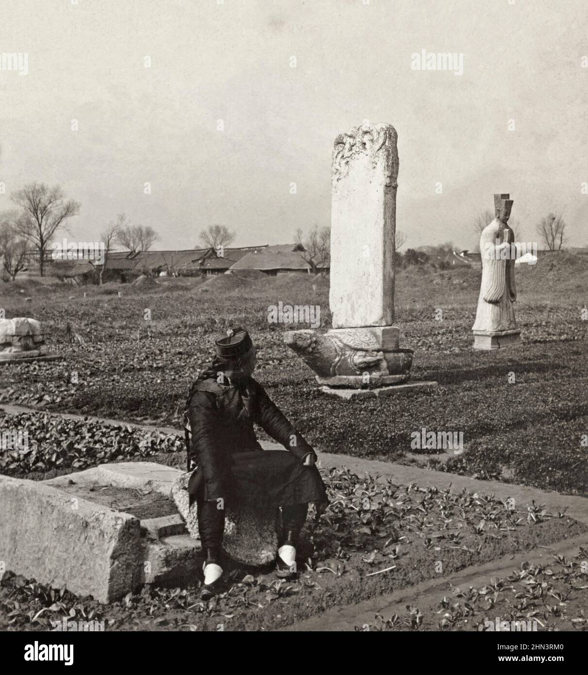 Photo d'époque de l'homme chinois en robe traditionnelle et avec file d'attente assise dans le potager dans un cimetière de la dynastie Ming. Chine du Nord. 1906 Banque D'Images