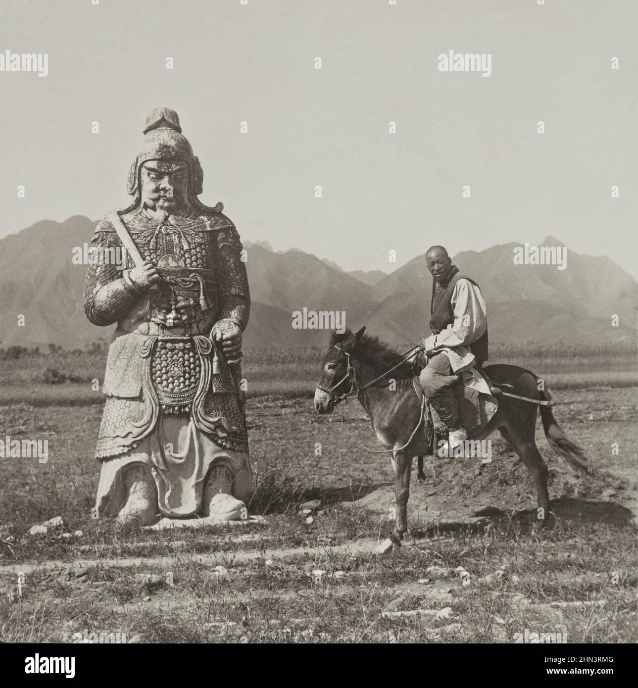 Photo d'époque d'un homme chinois en robe traditionnelle et avec file d'attente assise sur un âne près d'un soldat de pierre dans la célèbre avenue des animaux de pierre (Ming Banque D'Images