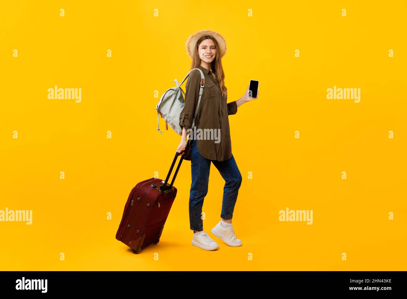 Femme touriste tenant smartphone posant avec des bagages sur fond jaune Banque D'Images