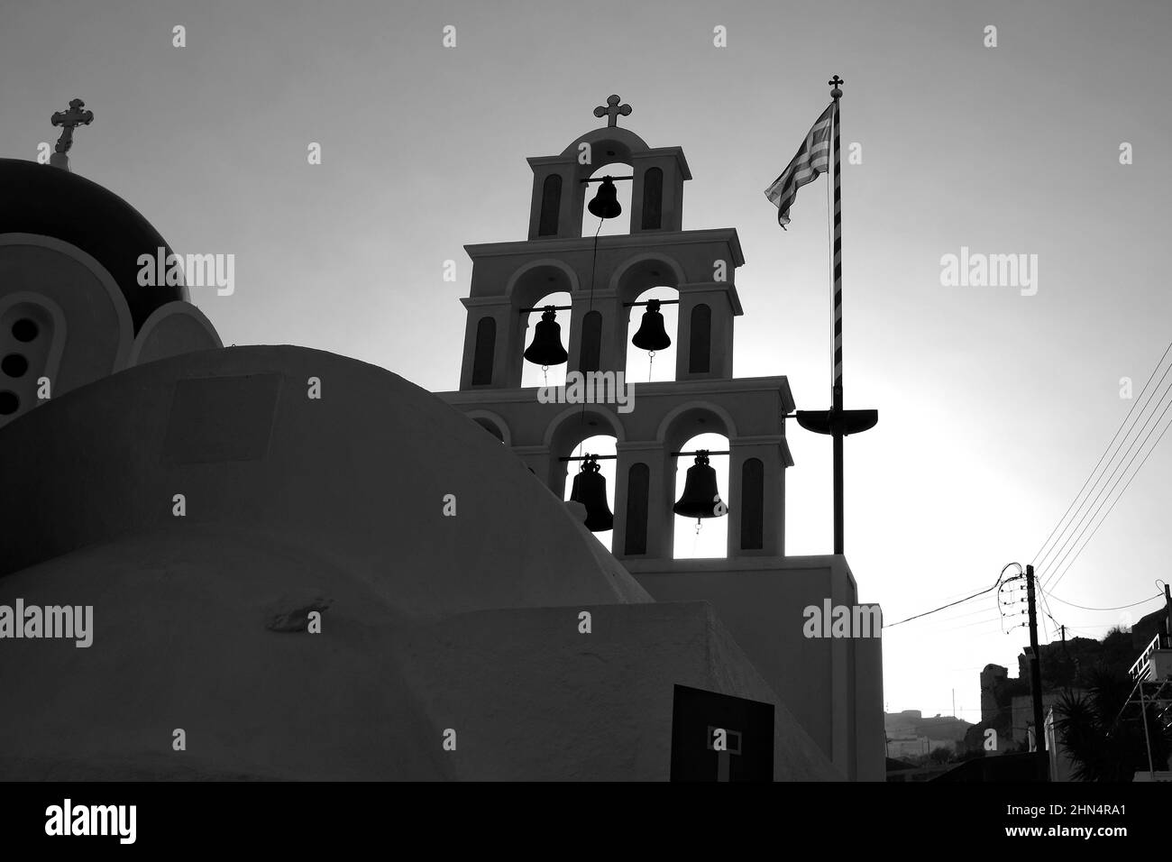 Étonnante église grecque orthodoxe blanche et bleue avec des croix religieuses, des cloches et le drapeau grec agitant dans l'air contre un ciel bleu à Santorin Banque D'Images