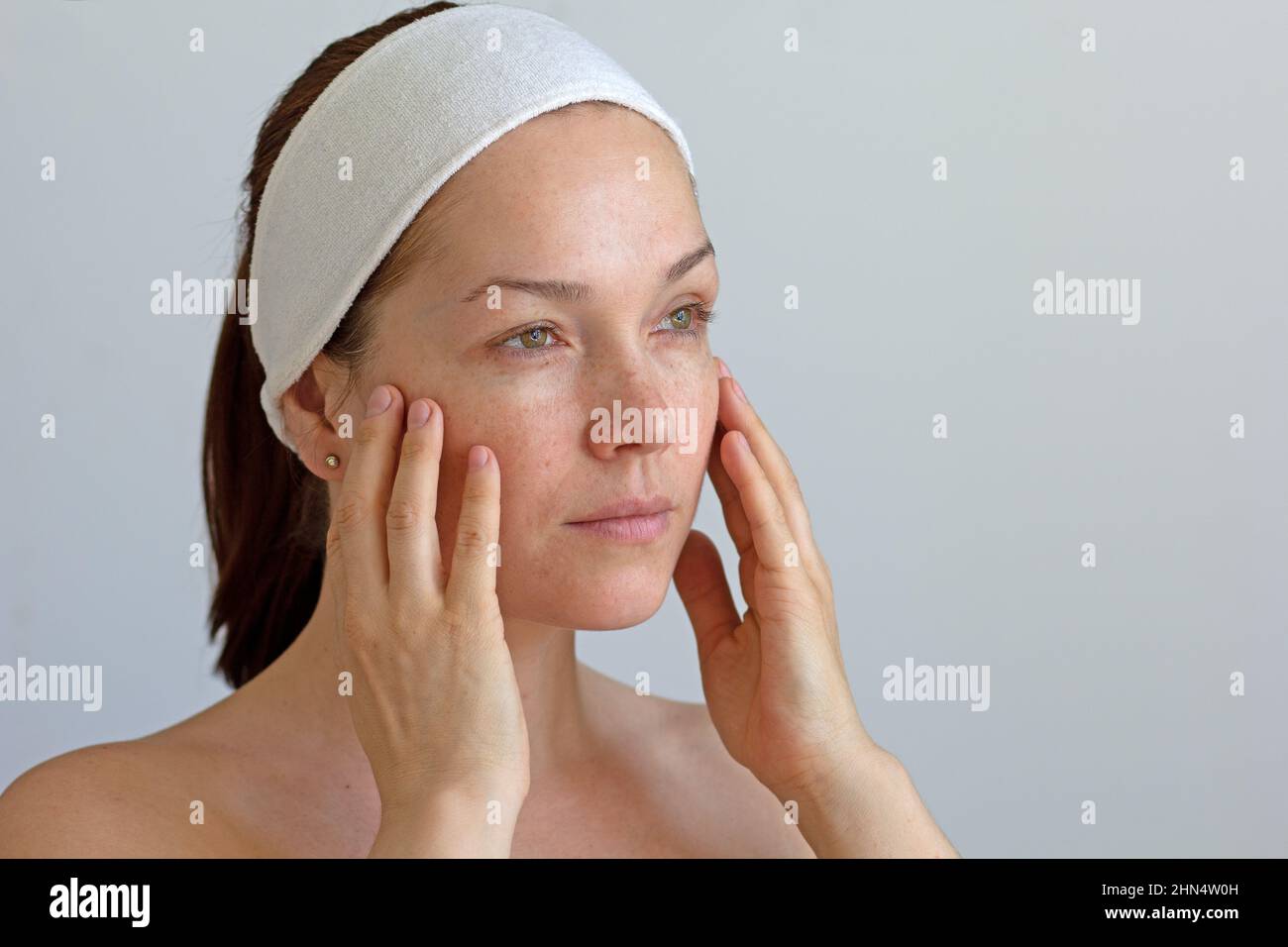 Portrait d'une femme d'âge moyen de race blanche sérieuse sans maquillage avec un groupe sur la tête touchant son visage en regardant de côté sur fond gris Banque D'Images