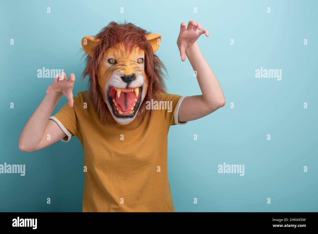 Jeune femme dans le masque de lion faisant des gestes effrayants d'attaque avec les mains, isolé sur fond bleu avec l'espace de copie. Banque D'Images