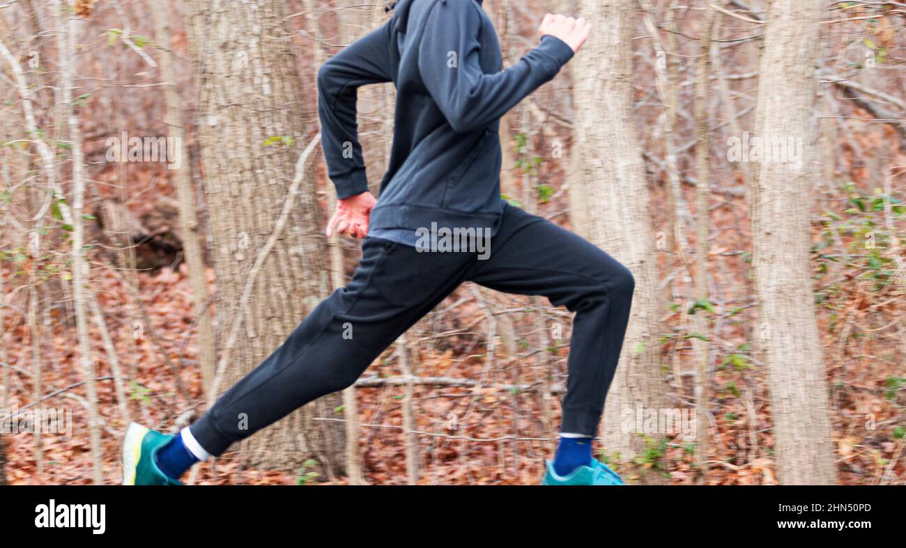 Un coureur de sexe masculin court rapidement sur un chemin dans les bois avec un arrière-plan flou d'arbres et de feuilles. Banque D'Images