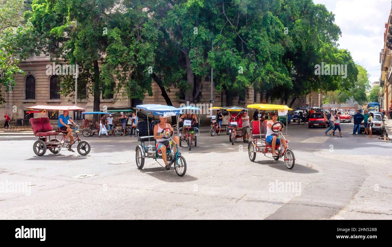 Un grand groupe de bicitaxis (pédicabs) se déplace dans une rue du quartier de la Vieille Havane. Ces véhicules sont des moyens de transport touristiques populaires dans la région. Banque D'Images