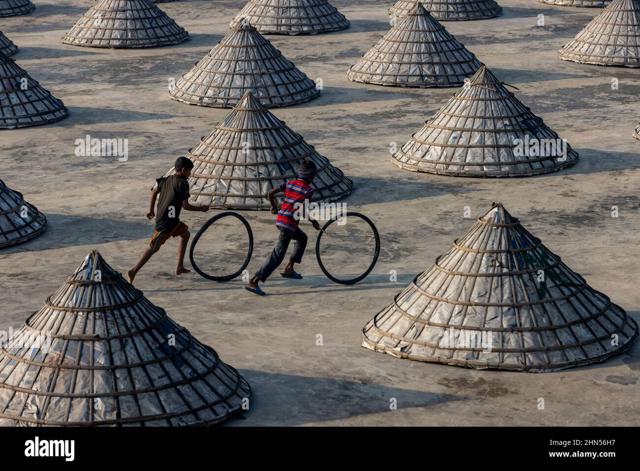 Des tas de rizières recouvertes de cônes dans la cour du moulin à riz de Brahmanbaria || Un employé sèche la riziculture dans la cour d'un moulin à riz de Brahmanbaria | Banque D'Images