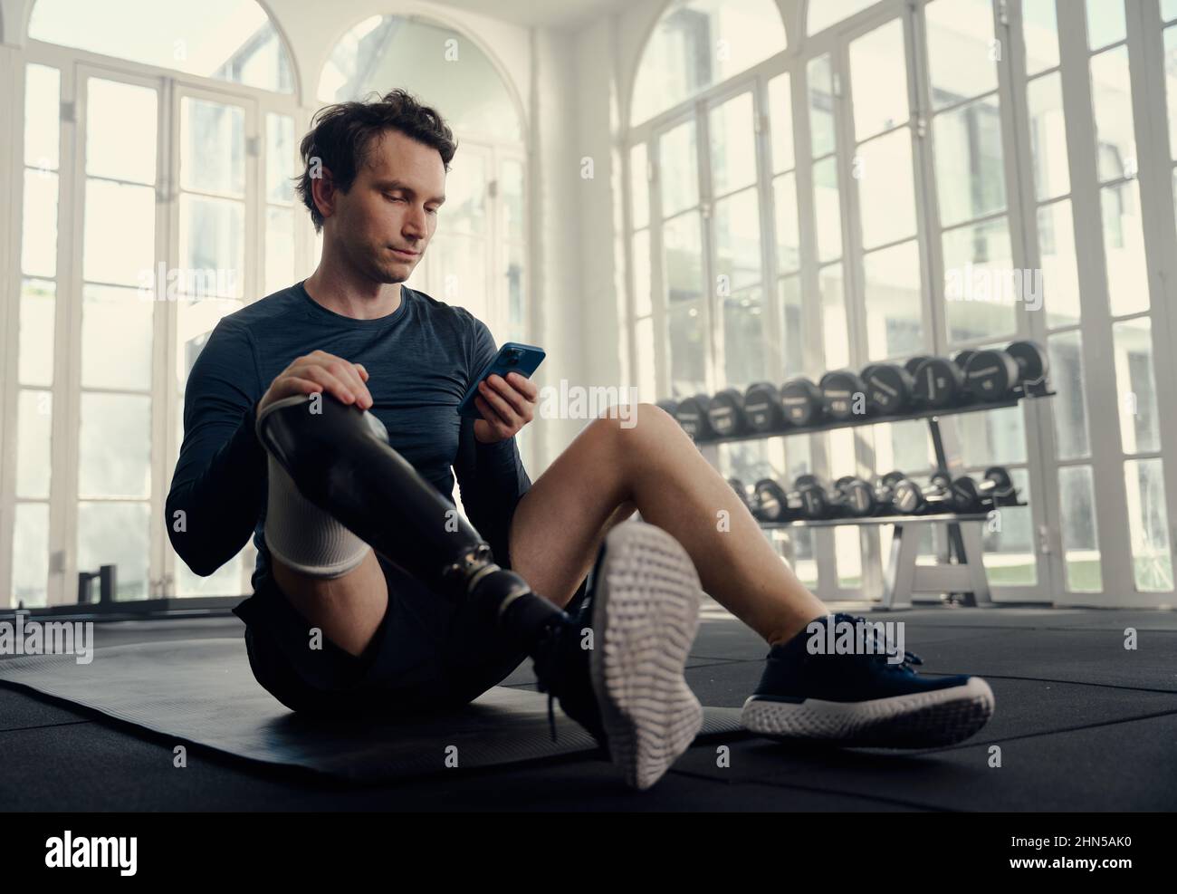Athlète paralympique sur son mobile dans l'entraînement de gym. Homme avec une jambe prothétique sur son téléphone cellulaire dans une salle de gym moderne Banque D'Images