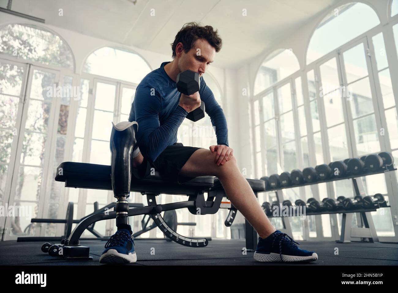 Athlète aux performances différentes faisant des boucles biceps dans la salle de gym en préparation aux Jeux paralympiques Banque D'Images