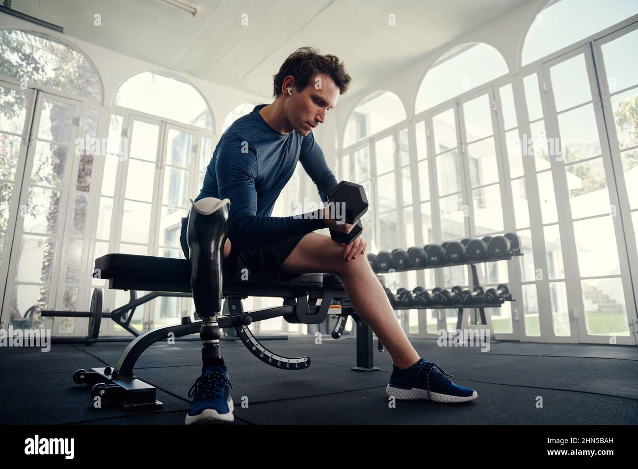Athlète handicapé faisant des boucles de biceps dans la salle de sport se préparant pour les Jeux paralympiques Banque D'Images