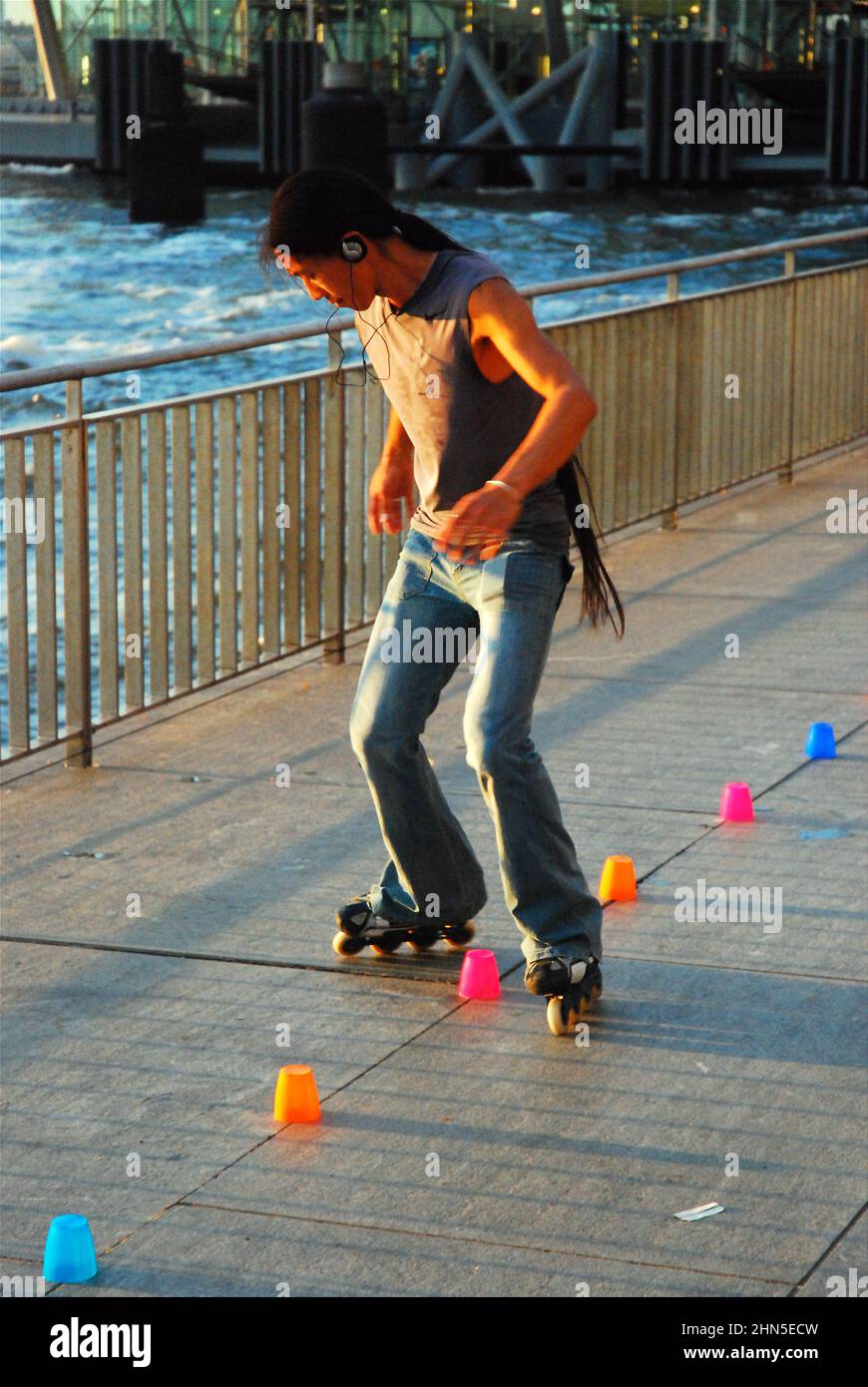 Un jeune homme pratique ses virages serrés tout en utilisant des patins en ligne, en utilisant des tasses pour marquer les virages à Battery Park, New York City Banque D'Images