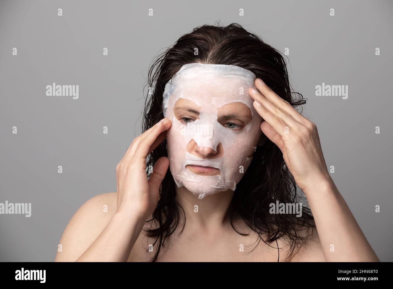 Femme appliquant un masque facial en feuilles ultra-fines pour nettoyer les pores, la sécheresse et les imperfections. Banque D'Images