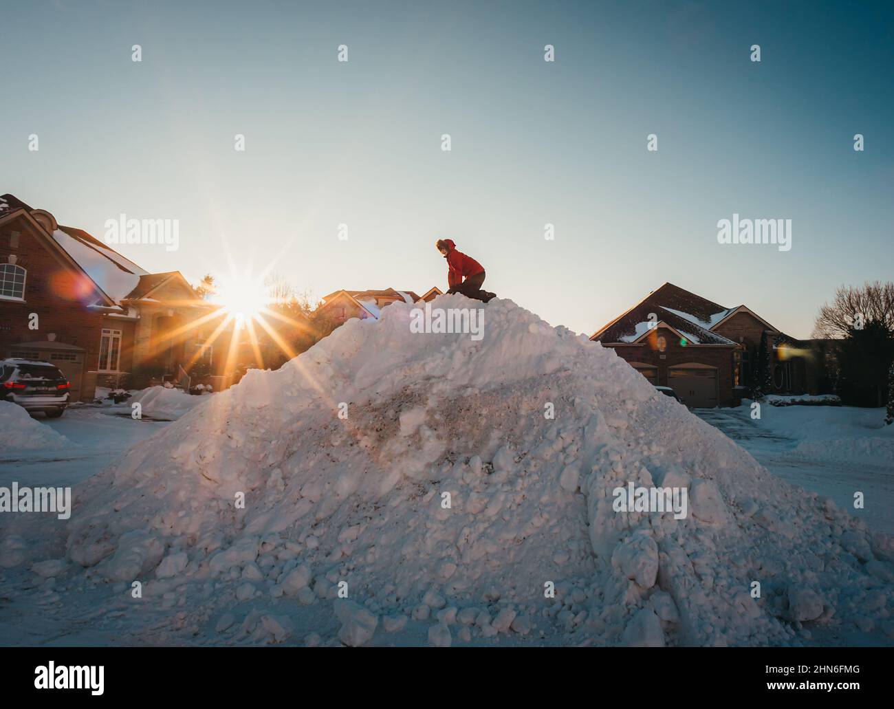 Enfant en veste d'hiver montant une grosse pile de neige dans une rue résidentielle. Banque D'Images