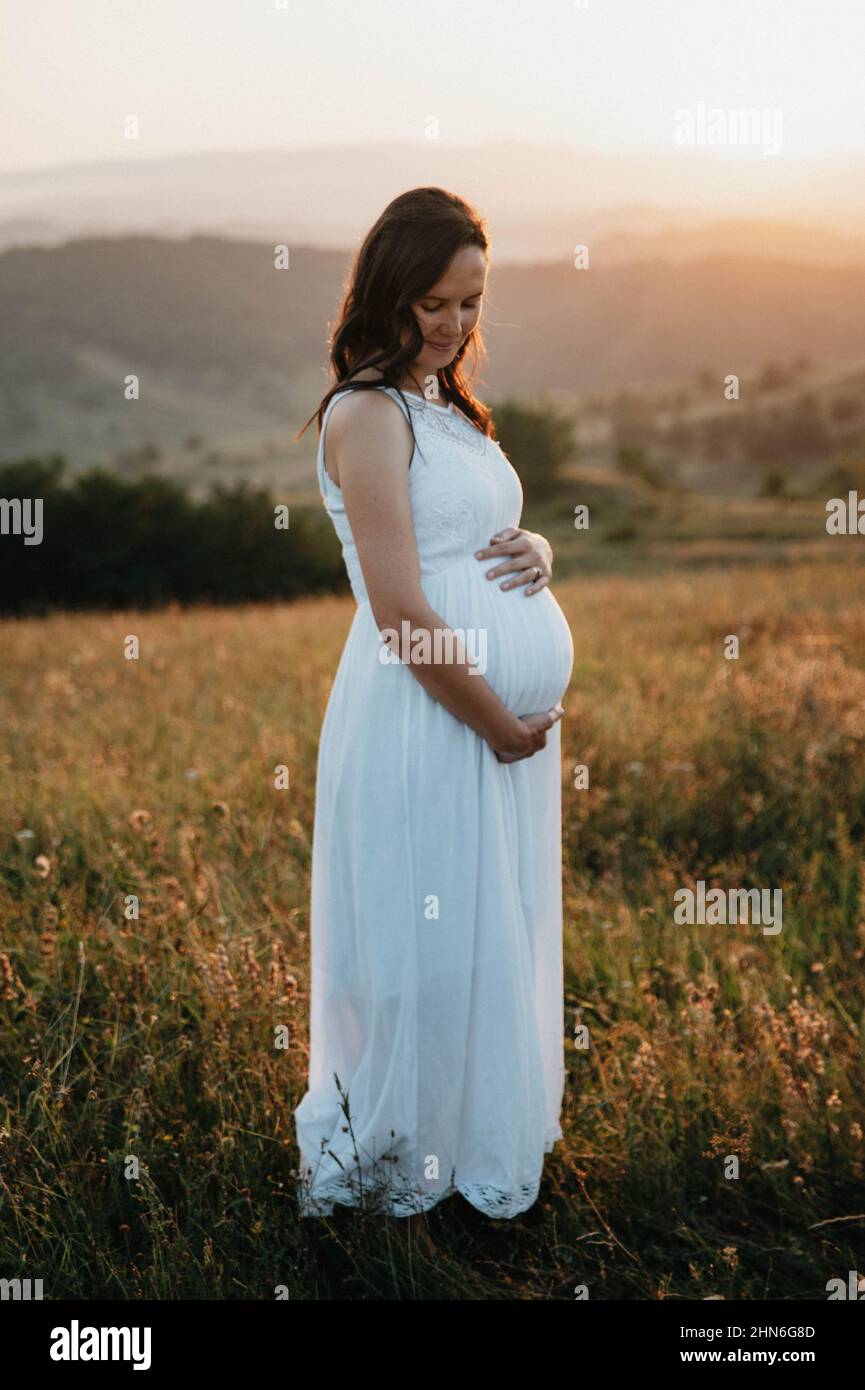 Belle femme enceinte tenant son ventre portant une robe blanche Banque D'Images