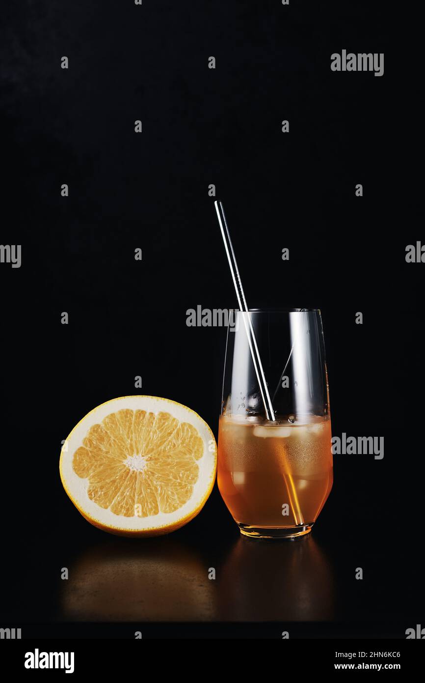 Cocktail de pamplemousse dans un verre avec une paille et un demi pamplemousse sur fond noir. Banque D'Images