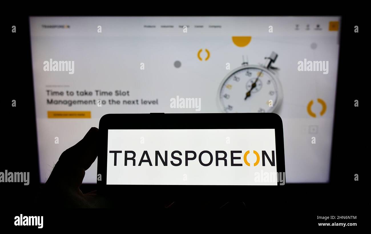 Personne tenant un téléphone portable avec le logo de la société allemande de logistique TRANSPOREON GmbH sur l'écran en face de la page web d'affaires. Mise au point sur l'affichage du téléphone. Banque D'Images Personne tenant un téléphone portable avec le logo de la société allemande de logistique TRANSPOREON GmbH sur l'écran en face de la page web d'affaires. Mise au point sur l'affichage du téléphone. Banque D'Images